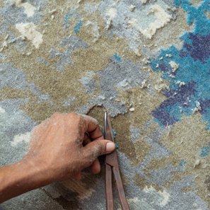 A hand trimming the pile of a blue and gold rug with shears