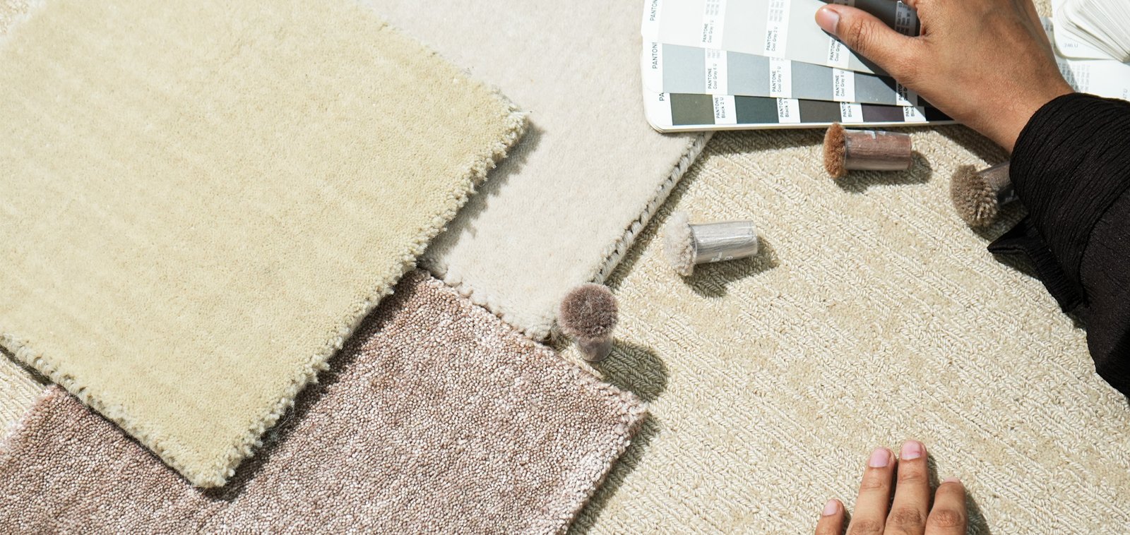 A hand holding a colour swatch over rug samples in cream, pink and beige