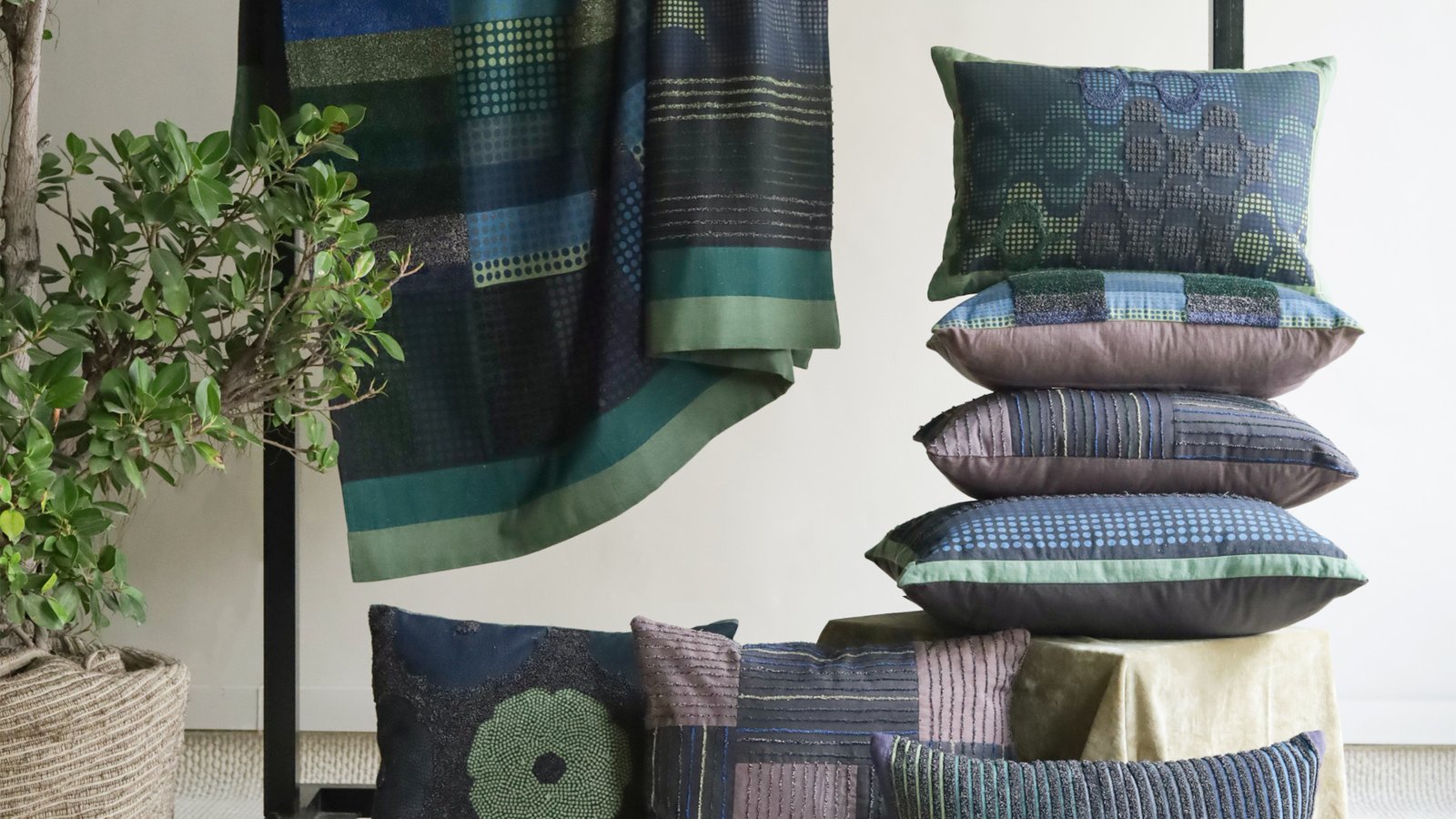 A stack of woven cushions in blue, green and pink beside a hanging patterned textile