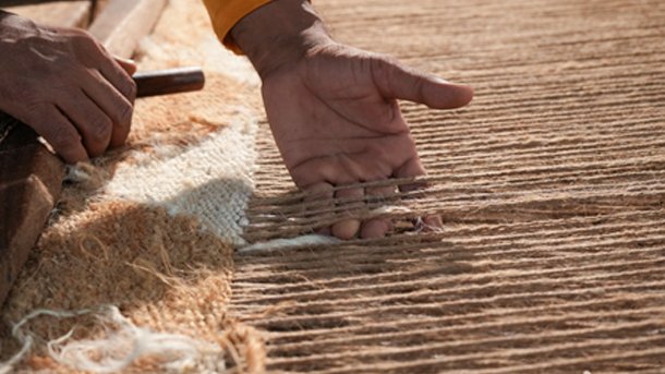 Hands beating the weft down with a comb on a rug in progress on the loom