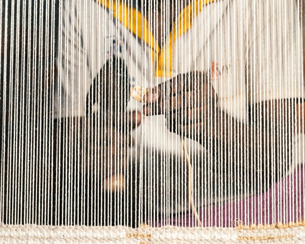 A weaver working coloured yarn through the warp threads of an upright loom