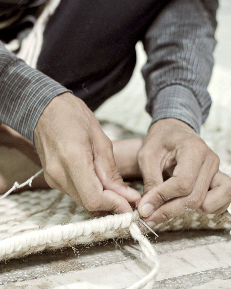 Close-up of hands binding the edge of a finished rug with white cord